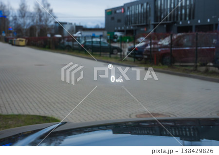 A luxury car HUD projects 0 kmh on a head up display and a speed limit icon on the windshield while idling by service bays and parked cars at a modern complex. A luxury car HUD projects 0 kmh on a head up display and a speed limit icon on the windshield while idling by service bays and parked cars at a modern complex. 138429826