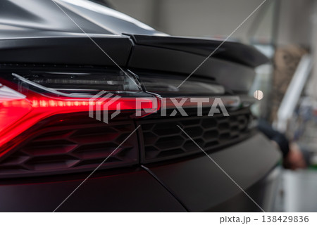 Tight view shows Lamborghini Urus style rear left corner in an indoor service bay, LED taillight illuminated, honeycomb grille texture, matte paint, soft industrial lighting 138429836