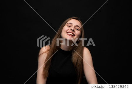 Happy young woman posing on a black background, expressing joy and laughter with a positive emotion and vibrant energy Happy young woman posing on a black background, expressing joy and laughter with a positive emotion and vibrant energy 138429843