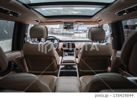 Wide interior view shows tan leather, chrome accents, panoramic roof, and Range Rover wheel and center stack, with workshop floor and service bays visible ahead. 138429844