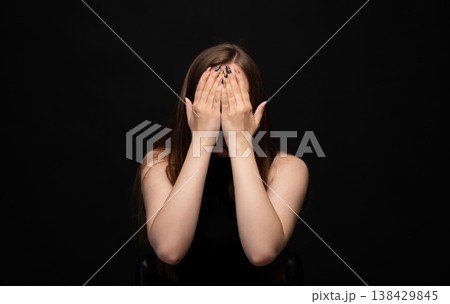 Young woman hiding face with hands, expressing shame, sadness, fear, anonymity, and privacy on black background Young woman hiding face with hands, expressing shame, sadness, fear, anonymity, and privacy on black background 138429845