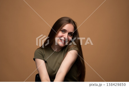 Young brunette woman with long hair smiling broadly while sitting in a studio, looking at camera with happy expression Young brunette woman with long hair smiling broadly while sitting in a studio, looking at camera with happy expression 138429850