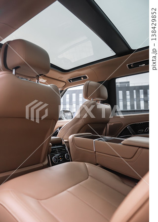 Tan leather interior with contrast stitching, panoramic glass roof, rear climate controls, wide center console, sculpted front seats, indoors in a luxury car workshop Tan leather interior with contrast stitching, panoramic glass roof, rear climate controls, wide center console, sculpted front seats, indoors in a luxury car workshop 138429852