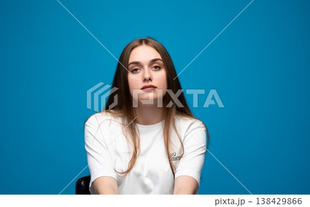 Young woman with long brown hair posing confidently in a white t-shirt against a vibrant blue studio background Young woman with long brown hair posing confidently in a white t-shirt against a vibrant blue studio background 138429866