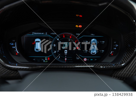 Close up digital cluster shows central tachometer and Park, 3D car diagrams, temperatures, and warnings, carbon fiber trim, luxury Lamborghini Urus SE interior in a workshop setting. Close up digital cluster shows central tachometer and Park, 3D car diagrams, temperatures, and warnings, carbon fiber trim, luxury Lamborghini Urus SE interior in a workshop setting. 138429938