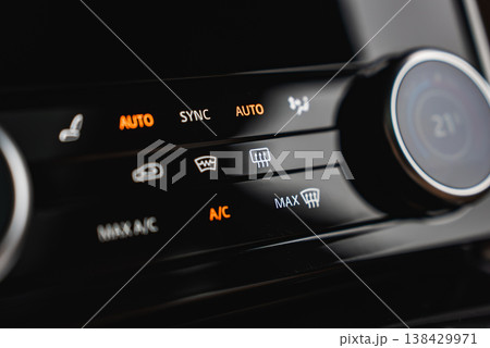 Illuminated AUTO, SYNC, A C, MAX defrost, and rear defog icons glow on a glossy panel with a rotary dial near 21 C, shot indoors in a high end workshop with shallow depth of field Illuminated AUTO, SYNC, A C, MAX defrost, and rear defog icons glow on a glossy panel with a rotary dial near 21 C, shot indoors in a high end workshop with shallow depth of field 138429971