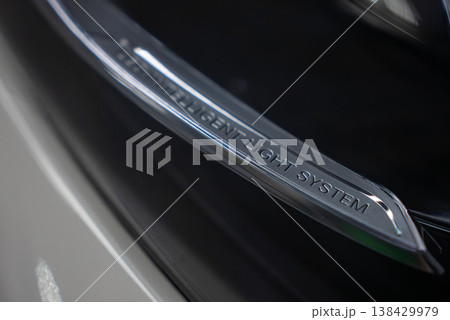 Tight close up shows Intelligent Light System text on a chrome headlight trim in a well lit workshop with Lamborghini Urus, Range Rover Autobiography, and Mercedes AMG present 138429979