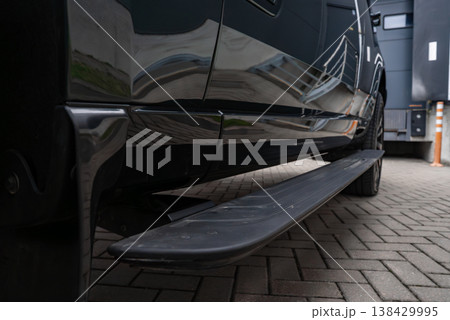 A low angle close up shows a luxury Range Rover SUV side step along a glossy black body, with light reflections, herringbone floor, and a service bay door in a workshop setting. 138429995