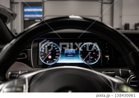 Driver's eye view shows twin gauges and steering wheel, speed and rpm flanking data screen, in a black dashboard within an upscale workshop under bright indoor light Driver's eye view shows twin gauges and steering wheel, speed and rpm flanking data screen, in a black dashboard within an upscale workshop under bright indoor light 138430061