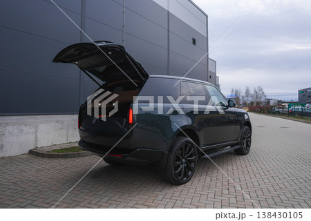 Black Range Rover Autobiography with tailgate open, vertical LED tail lights, black wheels, and tinted windows by gray metal warehouse in overcast daylight Black Range Rover Autobiography with tailgate open, vertical LED tail lights, black wheels, and tinted windows by gray metal warehouse in overcast daylight 138430105
