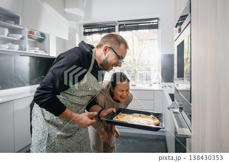 Happy couple laughing at freshly baked pizza in kitchen Happy couple laughing at freshly baked pizza in kitchen 138430353