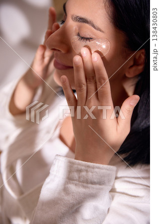 Woman applying under eye patches during skincare routine. Woman applying under eye patches during skincare routine. 138430803