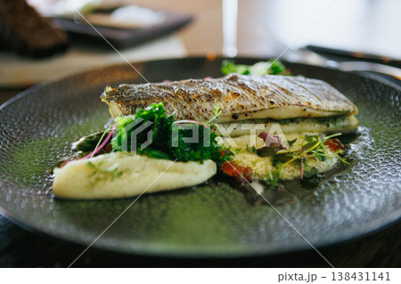 An artfully plated fish dish garnished with fresh greens and sauce, offering a delicious experience 138431141