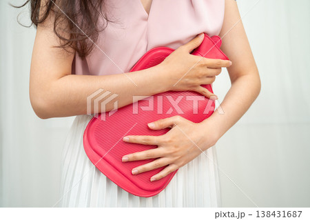 Woman using hot water bottle to relieve menstrual abdominal pain. 138431687