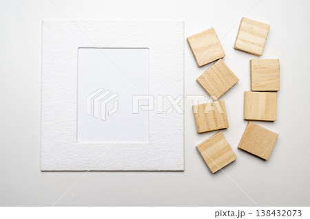 A high-angle minimalist composition featuring a textured white photo frame mat and several small wooden square tiles, offering ample copy space for creative design or text A high-angle minimalist composition featuring a textured white photo frame mat and several small wooden square tiles, offering ample copy space for creative design or text 138432073