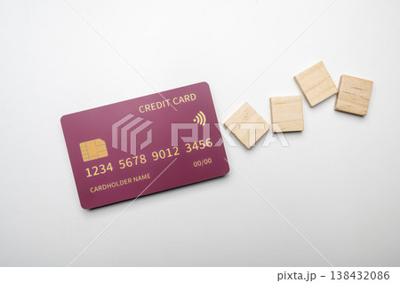 A high-angle shot of a burgundy credit card with gold details and wooden blocks on a minimalist white background, perfect for finance and payment concepts 138432086
