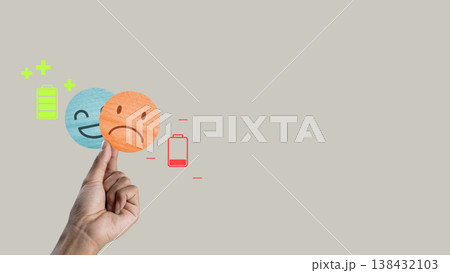Conceptual image of emotional health featuring a hand holding a sad emoji over a happy one. Icons of full and empty batteries illustrate energy levels and mental exhaustion Conceptual image of emotional health featuring a hand holding a sad emoji over a happy one. Icons of full and empty batteries illustrate energy levels and mental exhaustion 138432103