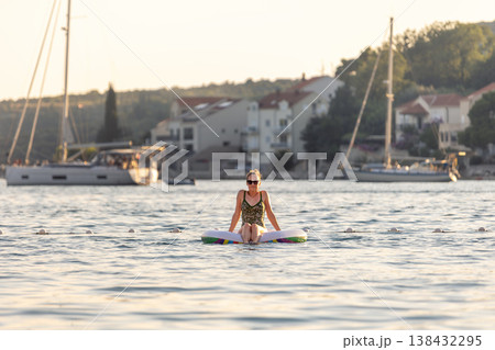 Scenic view woman relax alone inflatable raft calm sea coastal village marina sailboats warm sunset light. Peaceful summer atmosphere solo vacation lifestyle freedom relaxation mediterranean scenery Scenic view woman relax alone inflatable raft calm sea coastal village marina sailboats warm sunset light. Peaceful summer atmosphere solo vacation lifestyle freedom relaxation mediterranean scenery 138432295