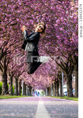 Dynamic scenic young adult pretty happy woman enjoy walking spring city street blooming pink cherry trees alley background in Magdeburg city. Female person joyful carefree portrait smiling outdoors 138432374