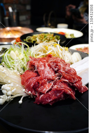 Fresh raw beef bulgogi with assorted vegetables including green onions, bean sprouts, and enoki mushrooms on a black plate, traditional Korean marinated beef preparation before cooking 138432808