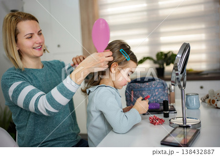 Mother brushing daughter's hair with child applying lipstick Mother brushing daughter's hair with child applying lipstick 138432887