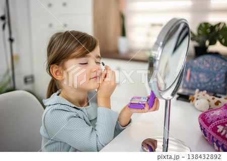 Little girl playing with eyeshadow in front of makeup mirror 138432892