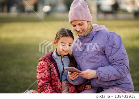 Mother and daughter bonding over smartphone in park 138432915