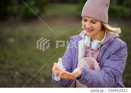Smiling woman spraying hand sanitizer on her palm outdoors 138432921
