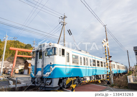 【牟岐線】神社の鳥居の横を通過する普通列車 138433263