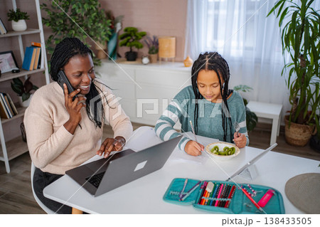 Mother talking on phone and using laptop while daughter studying Mother talking on phone and using laptop while daughter studying 138433505