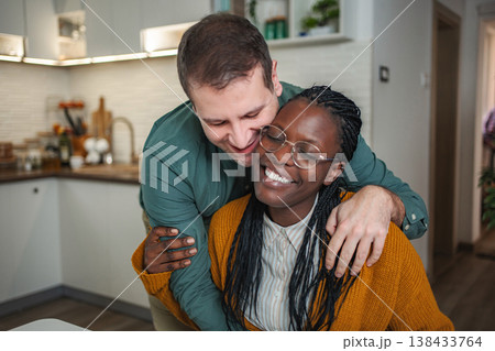 Happy interracial couple hugging in home kitchen 138433764