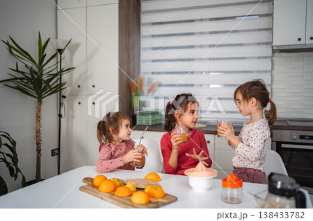 Girls enjoying fresh orange juice in kitchen Girls enjoying fresh orange juice in kitchen 138433782