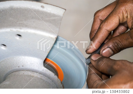 Skilled operator performing a manual regrinding process on a lathe cutting tool using an abrasive stone grinding wheel. Skilled operator performing a manual regrinding process on a lathe cutting tool using an abrasive stone grinding wheel. 138433802