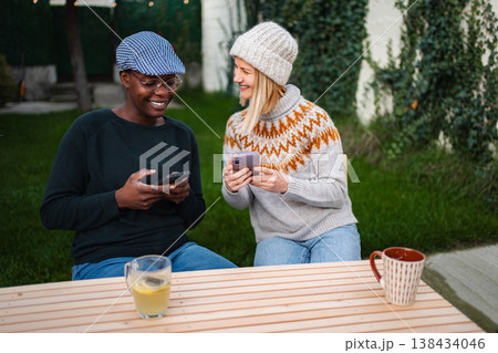 Diverse women friends sitting outdoors laughing using mobile phones Diverse women friends sitting outdoors laughing using mobile phones 138434046