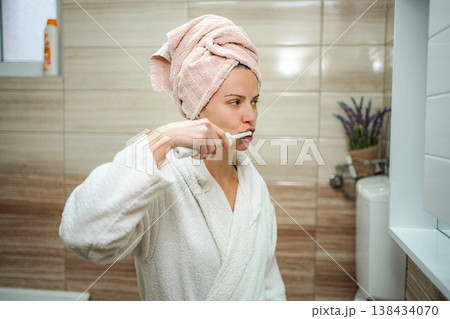 Woman brushing teeth with electric toothbrush in bathroom Woman brushing teeth with electric toothbrush in bathroom 138434070