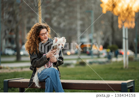 Young adult woman using smartphone with dog on park bench Young adult woman using smartphone with dog on park bench 138434158