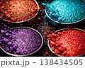 Close-up of vibrant, shimmering loose eyeshadow pigments in four colorful pots 138434505