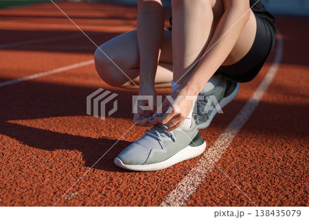 Close up of woman tying running shoe laces on outdoor track before exercise, fitness preparation Close up of woman tying running shoe laces on outdoor track before exercise, fitness preparation 138435079
