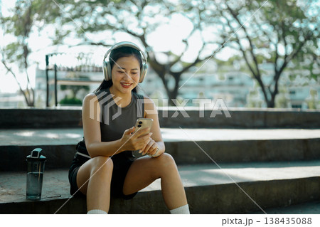 Smiling woman resting and listening to music on smartphone outdoor workout break in park Smiling woman resting and listening to music on smartphone outdoor workout break in park 138435088
