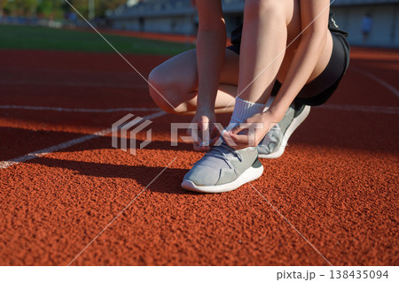 Close up of woman tying running shoe laces on outdoor track before exercise, fitness preparation 138435094
