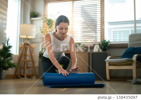 Woman folding, rolling exercise mat before working out at home. rolling Yoga mat after training healthy lifestyle Woman folding, rolling exercise mat before working out at home. rolling Yoga mat after training healthy lifestyle 138435097