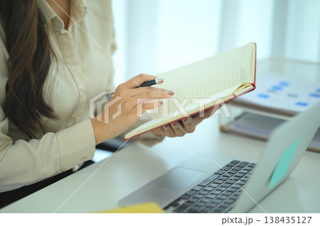 Close up of businesswoman reviewing notebook at desk Close up of businesswoman reviewing notebook at desk 138435127