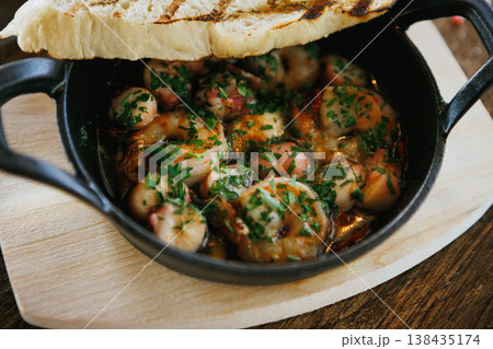 A skillet of shrimp and fresh bread rests on a wooden table A skillet of shrimp and fresh bread rests on a wooden table 138435174