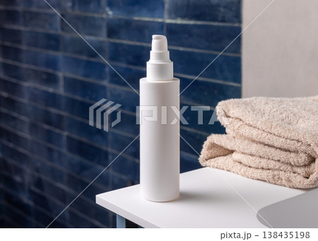 White pump cosmetic bottle near beige bath towel in dark blue bathroom, cosmetic mockup 138435198