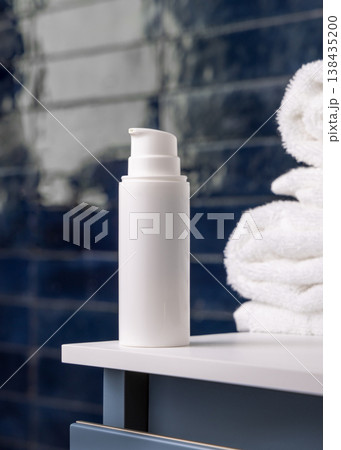 White pump cosmetic bottle near white bath towel in dark blue bathroom, cosmetic mockup 138435200