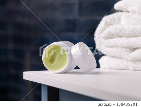Opened handmade lip balm jar in blue bathroom with towel. Blank lid cosmetic mockup 138435201