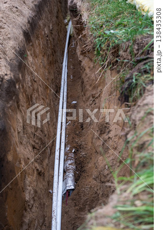 Deep trench digging for water line, laying insulated pipes, plumbing thermal protection, installation site, groundwork for house utility connections. 138435308