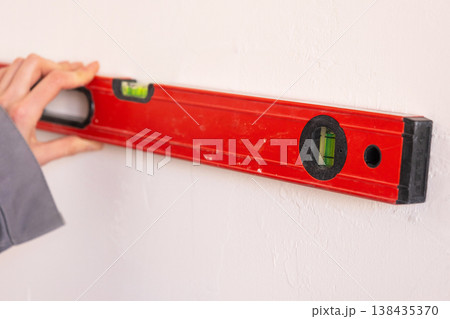 Professional uses building level for line marking, wall layout preparation, construction, accurate alignment, renovation start, interior setup. Professional uses building level for line marking, wall layout preparation, construction, accurate alignment, renovation start, interior setup. 138435370
