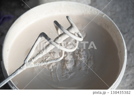 Wet plaster mixture being mixed by drill mixer in bucket, construction renovation, wall repair prep, craftsmen tool for surface and coating works. Wet plaster mixture being mixed by drill mixer in bucket, construction renovation, wall repair prep, craftsmen tool for surface and coating works. 138435382