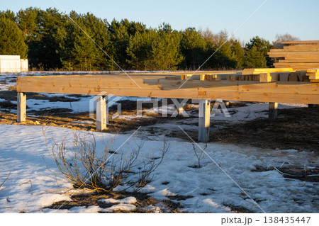 Timber frame base on piles, early construction stage, structural setup, wood beams, frame mounting process, carpentry, foundation wood, outdoor worksite. 138435447